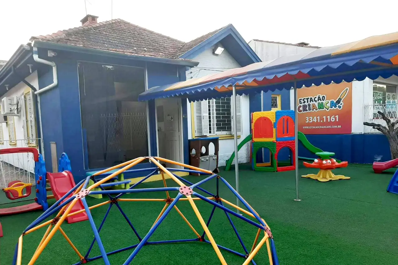 Fachada azul da Estação Criança, com pátio gramado e brinquedos coloridos