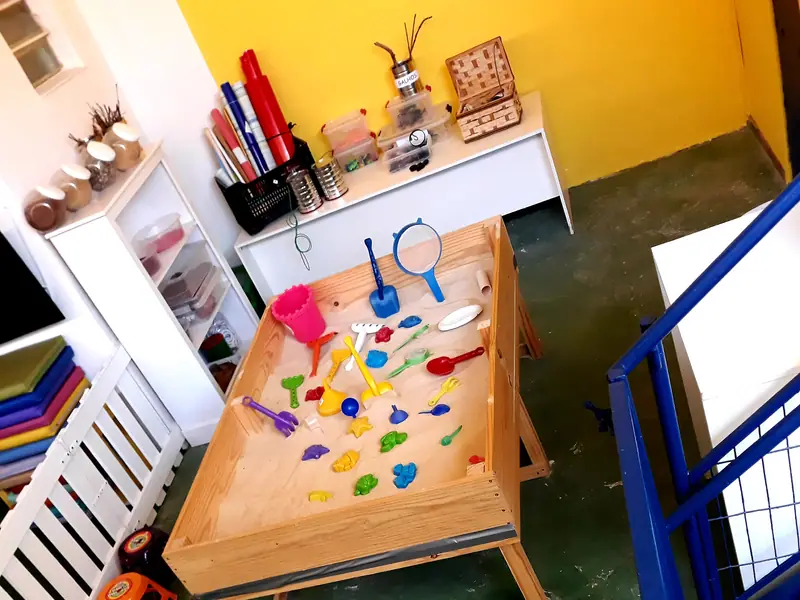 Mesa de atividades com brinquedos de madeira, materiais para criar e cadeirinhas na altura das crianças